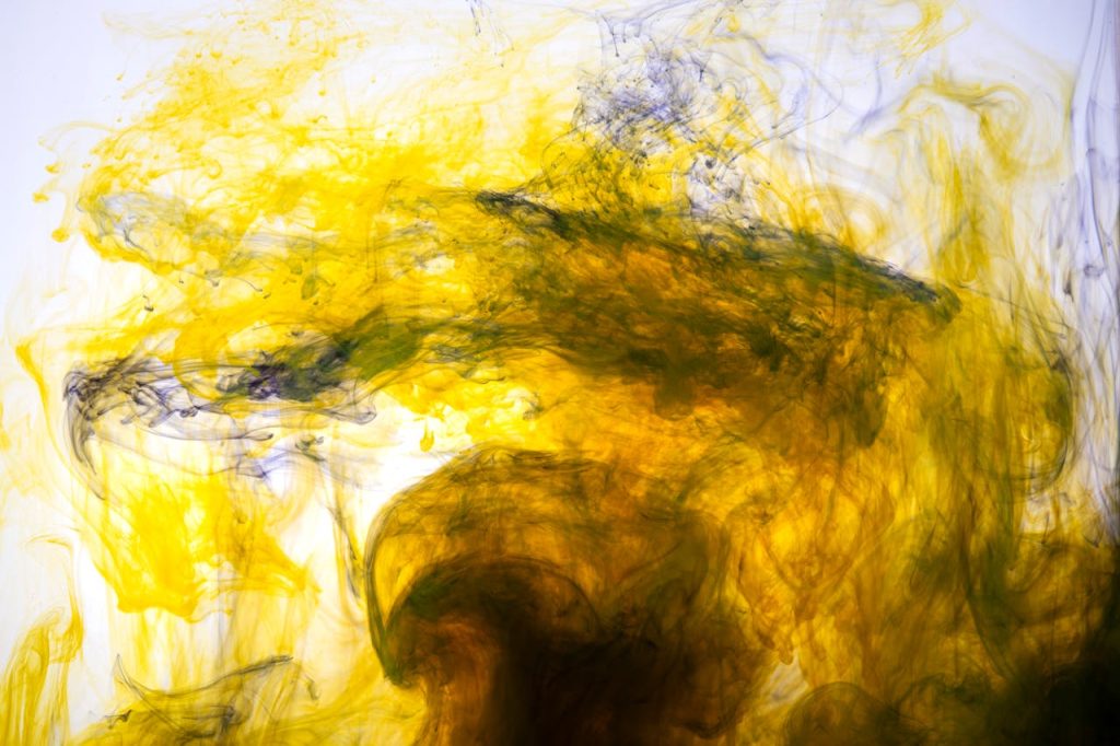 Dynamic abstract image of yellow ink swirling in water, creating mesmerising patterns.
